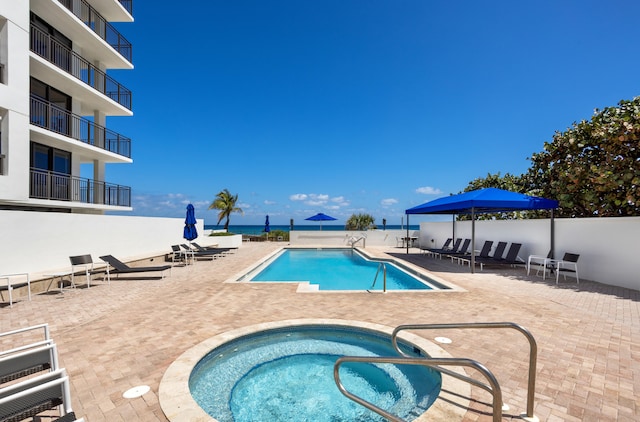 view of swimming pool featuring a water view, a patio area, and a community hot tub