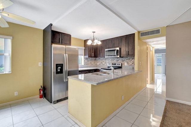 kitchen featuring sink, stainless steel appliances, light stone countertops, decorative light fixtures, and kitchen peninsula