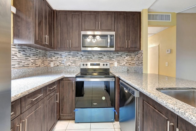 kitchen with dark brown cabinets, stainless steel appliances, tasteful backsplash, light stone counters, and light tile patterned flooring