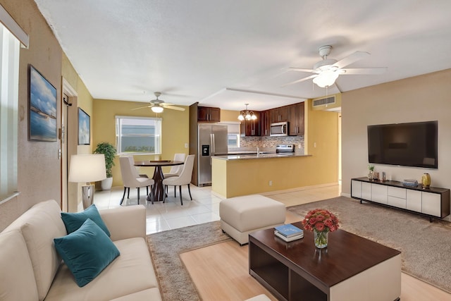 tiled living room with ceiling fan with notable chandelier