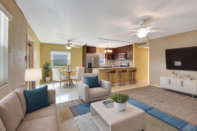 tiled living room with ceiling fan with notable chandelier