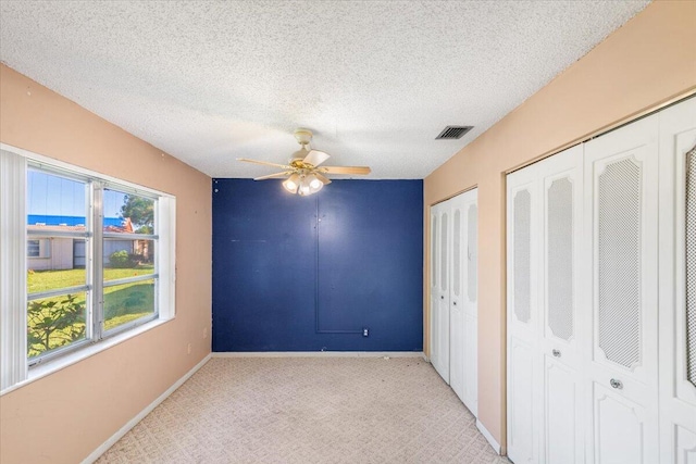 unfurnished bedroom with a textured ceiling, ceiling fan, light colored carpet, and two closets