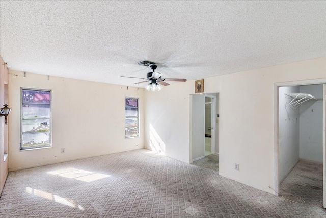 unfurnished bedroom with ceiling fan, a textured ceiling, a walk in closet, light carpet, and a closet