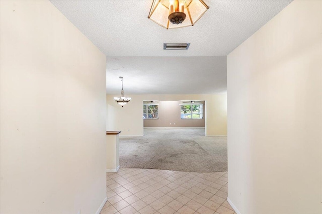 hallway with light carpet, a textured ceiling, and a notable chandelier