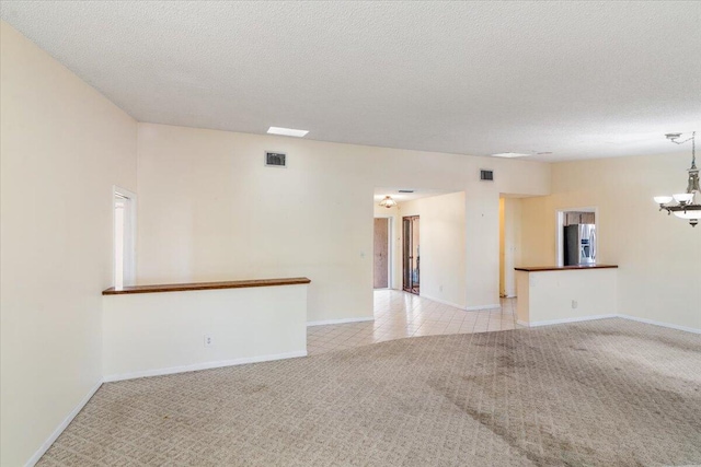 carpeted empty room with a textured ceiling and an inviting chandelier