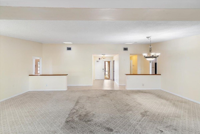 carpeted empty room featuring a chandelier and a textured ceiling