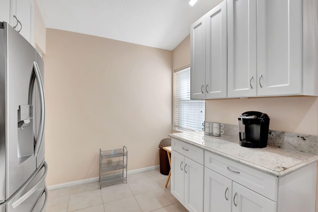 kitchen featuring stainless steel fridge, white cabinets, light stone countertops, and light tile patterned floors