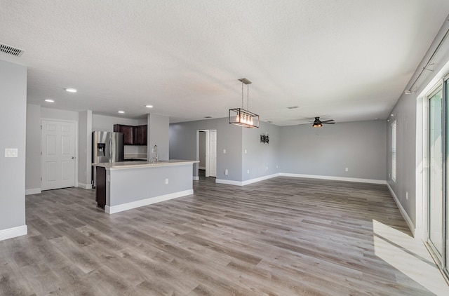 unfurnished living room with light wood-type flooring, sink, ceiling fan, and a textured ceiling