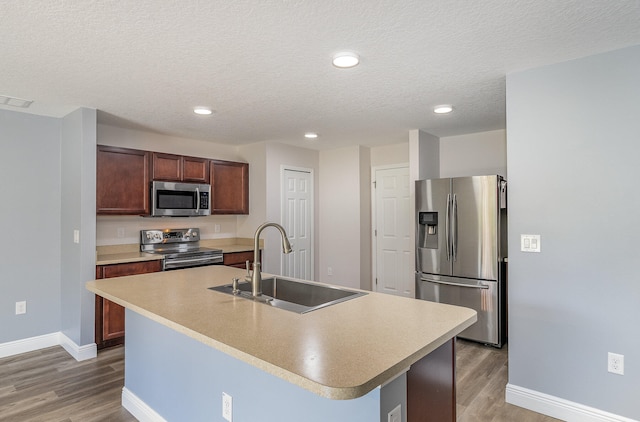 kitchen with hardwood / wood-style floors, a textured ceiling, sink, an island with sink, and appliances with stainless steel finishes