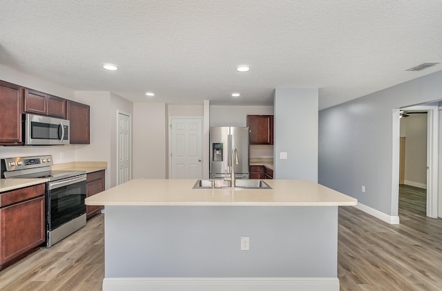 kitchen featuring a textured ceiling, light wood-type flooring, stainless steel appliances, and a center island with sink