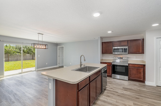 kitchen with appliances with stainless steel finishes, decorative light fixtures, light hardwood / wood-style flooring, sink, and a kitchen island with sink