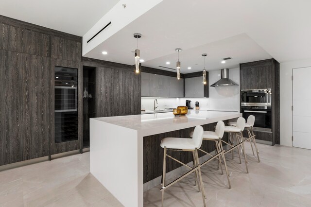 kitchen featuring a large island, sink, hanging light fixtures, wall chimney range hood, and a breakfast bar