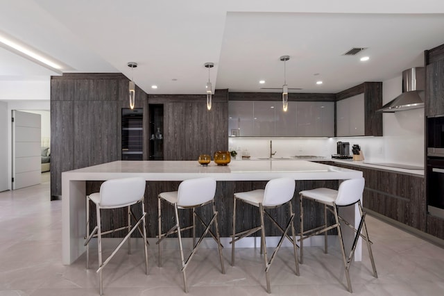 kitchen featuring wall chimney exhaust hood, a spacious island, and decorative light fixtures