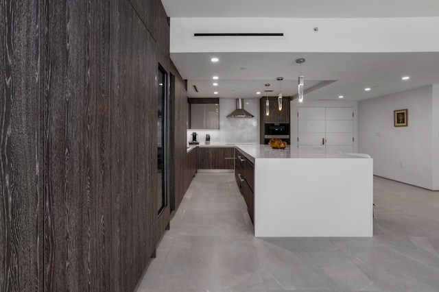 kitchen featuring dark brown cabinetry, a large island, wall chimney exhaust hood, tasteful backsplash, and decorative light fixtures