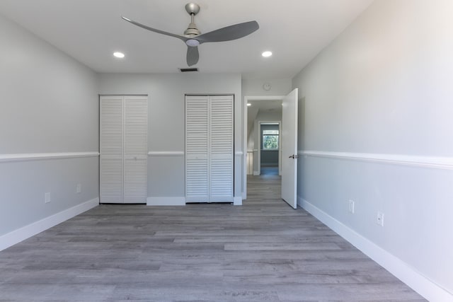 unfurnished bedroom with wood-type flooring, multiple closets, and ceiling fan