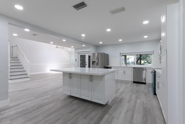 kitchen with ceiling fan, white cabinetry, stainless steel appliances, a center island, and light hardwood / wood-style floors