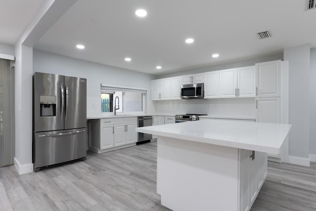 kitchen with appliances with stainless steel finishes, a kitchen island, light wood-type flooring, and white cabinetry