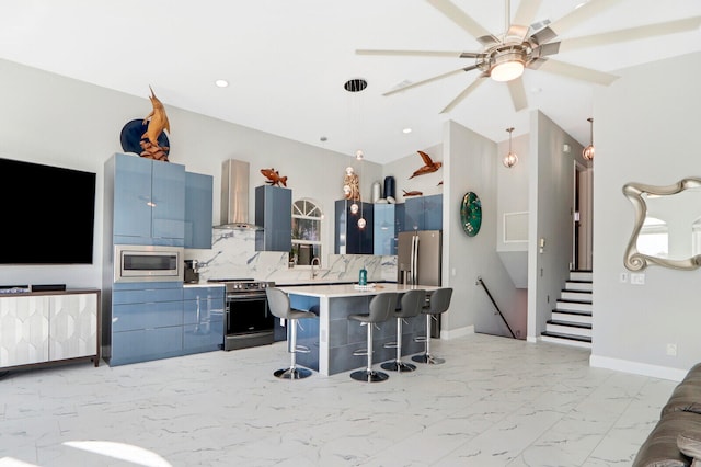 kitchen featuring wall chimney exhaust hood, a kitchen breakfast bar, decorative light fixtures, a kitchen island, and appliances with stainless steel finishes