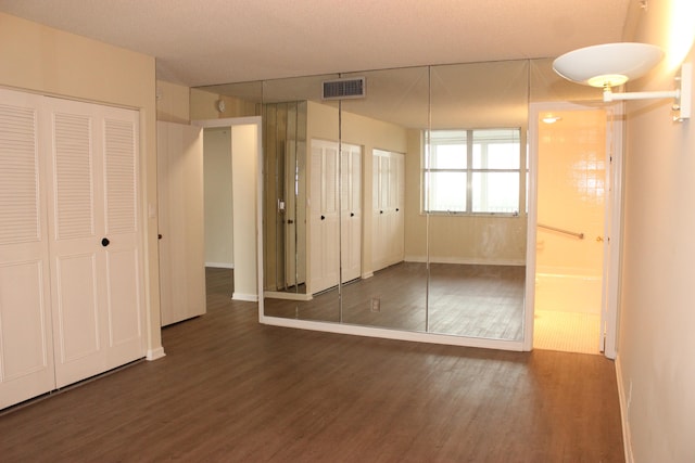 unfurnished bedroom featuring a textured ceiling, ensuite bath, and dark hardwood / wood-style flooring