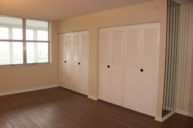 unfurnished bedroom featuring multiple closets, dark hardwood / wood-style flooring, and a textured ceiling