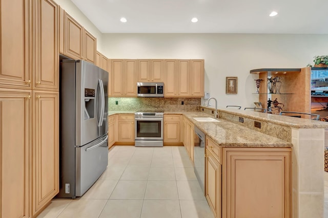 kitchen featuring kitchen peninsula, light stone counters, light brown cabinetry, stainless steel appliances, and sink