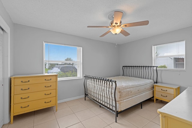 bedroom with a closet, light tile patterned floors, a textured ceiling, and ceiling fan