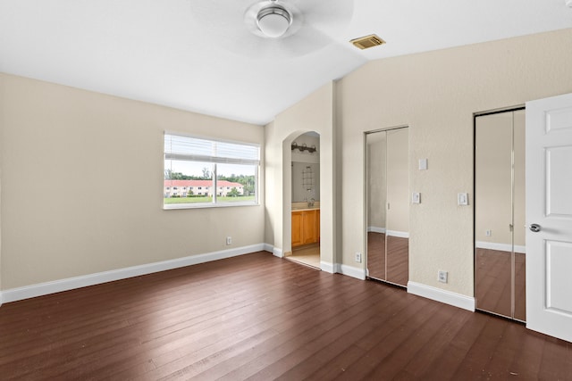 unfurnished bedroom with connected bathroom, two closets, dark wood-type flooring, and vaulted ceiling