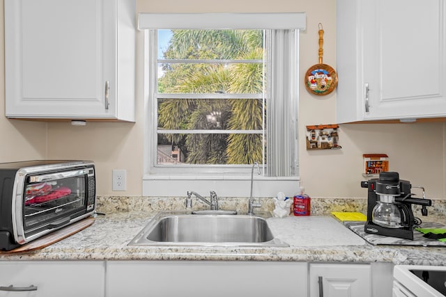 kitchen with white cabinets, sink, and light stone counters