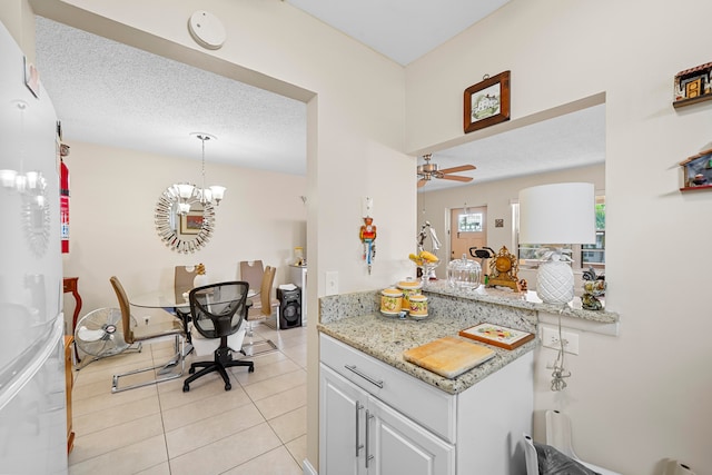 kitchen featuring light stone countertops, light tile patterned floors, white cabinets, a textured ceiling, and ceiling fan with notable chandelier