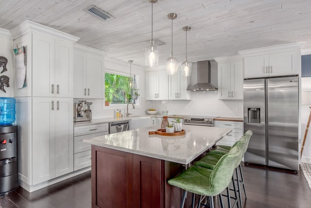 kitchen featuring wall chimney range hood, decorative light fixtures, dark hardwood / wood-style floors, white cabinets, and appliances with stainless steel finishes