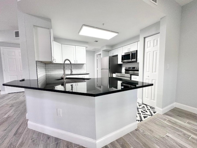 kitchen featuring kitchen peninsula, decorative backsplash, sink, stainless steel appliances, and white cabinets