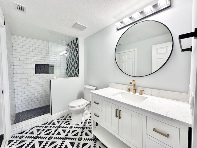 bathroom with toilet, tiled shower, tile patterned floors, a textured ceiling, and vanity