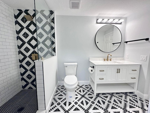 bathroom with toilet, vanity, a textured ceiling, and a tile shower