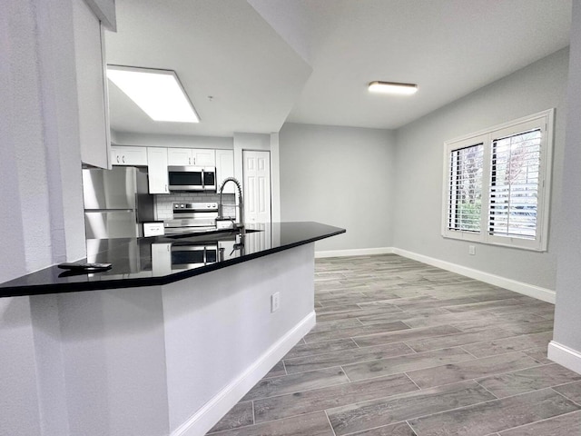 kitchen with kitchen peninsula, stainless steel appliances, decorative backsplash, light wood-type flooring, and white cabinets