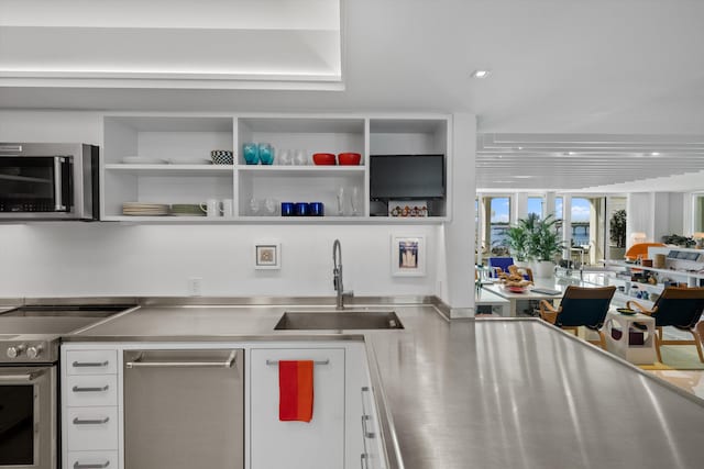 kitchen with stainless steel appliances, stainless steel counters, white cabinets, and sink