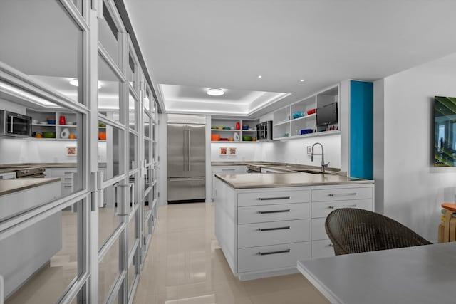 kitchen featuring white cabinets, stainless steel appliances, a sink, open shelves, and light countertops