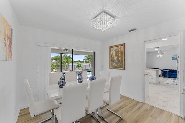 dining area with ceiling fan with notable chandelier and light wood-type flooring