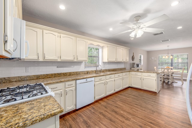 kitchen featuring white appliances, decorative light fixtures, sink, kitchen peninsula, and hardwood / wood-style flooring