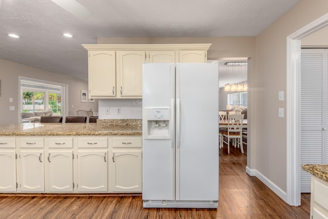 kitchen featuring white fridge with ice dispenser, hardwood / wood-style flooring, light stone countertops, and a textured ceiling