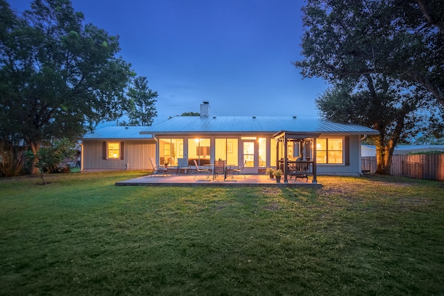 back house at dusk featuring a yard and a patio