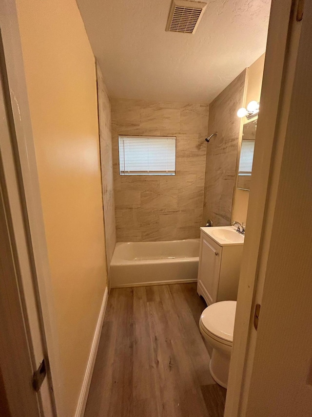 full bathroom with toilet, tiled shower / bath combo, hardwood / wood-style flooring, vanity, and a textured ceiling