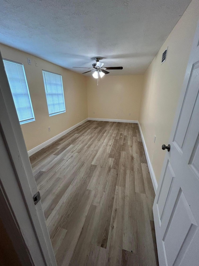 spare room with a textured ceiling, ceiling fan, and light hardwood / wood-style flooring