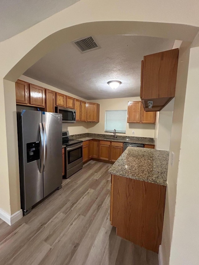 kitchen featuring sink, a textured ceiling, stone counters, appliances with stainless steel finishes, and light wood-type flooring