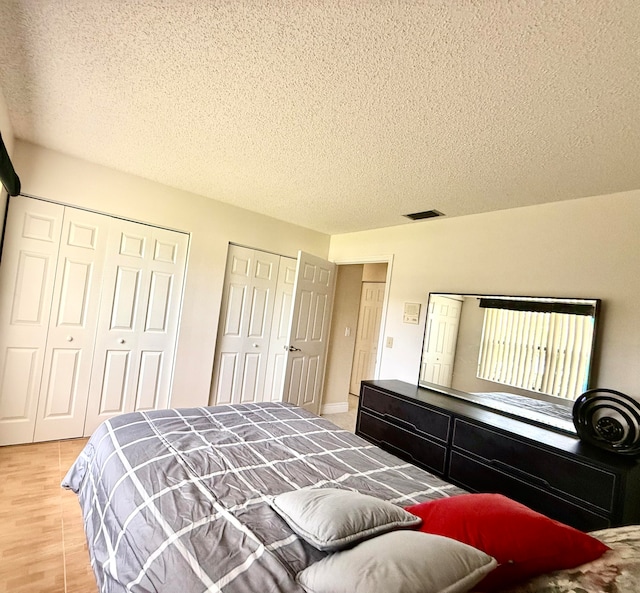 bedroom featuring light hardwood / wood-style flooring, a textured ceiling, and multiple closets