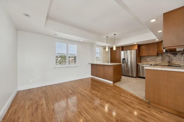 kitchen featuring hanging light fixtures, backsplash, a raised ceiling, light hardwood / wood-style flooring, and stainless steel appliances