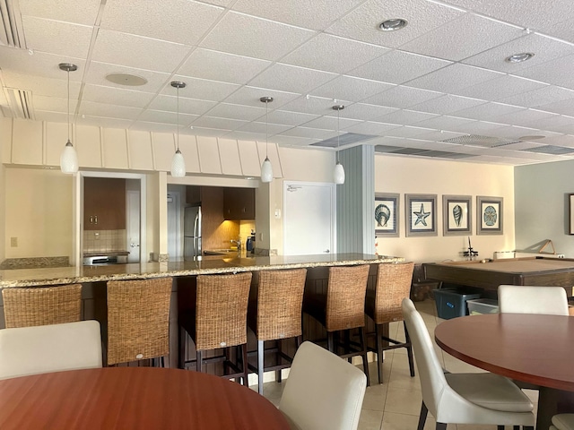 interior space with a paneled ceiling, stainless steel fridge, pendant lighting, and light tile patterned floors