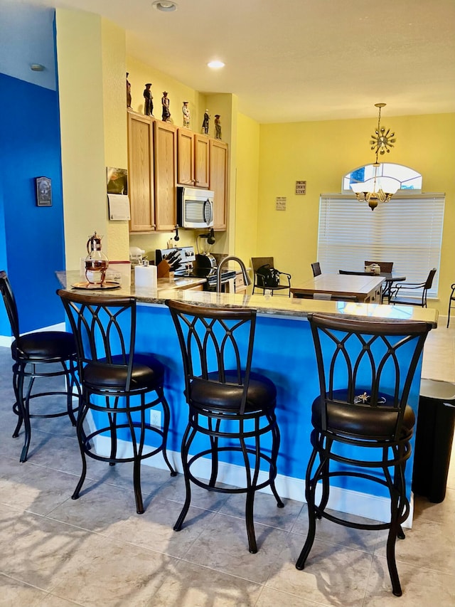 kitchen with stainless steel appliances, kitchen peninsula, hanging light fixtures, an inviting chandelier, and a kitchen breakfast bar