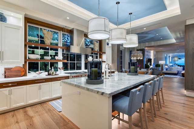 kitchen featuring an island with sink, a breakfast bar, decorative light fixtures, a raised ceiling, and white cabinetry