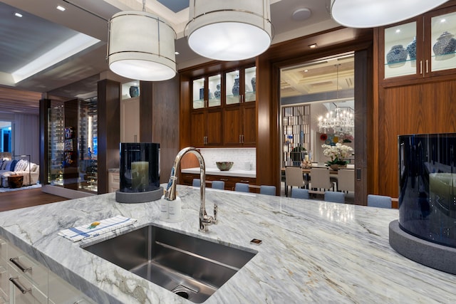 kitchen with decorative backsplash, light stone counters, an inviting chandelier, wooden walls, and sink