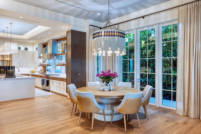 dining room featuring sink, a chandelier, light hardwood / wood-style flooring, and a raised ceiling